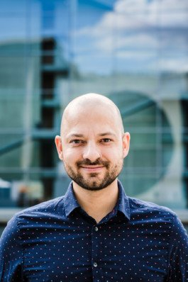 Portrait von einem vollbärtigen Mann mit kurzen Haaren, der in die Kamera lächelt. Er trägt ein Shirt mit einem Fahrrad.