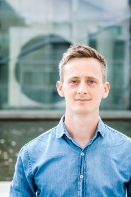 Portrait von einem vollbärtigen Mann mit kurzen Haaren, der in die Kamera lächelt. Er trägt ein Shirt mit einem Fahrrad.