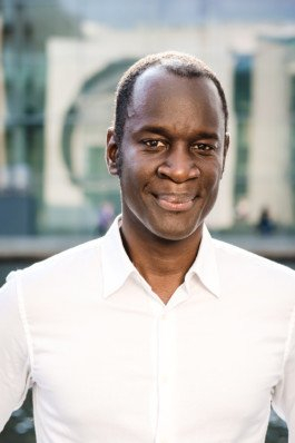 Portrait von einem vollbärtigen Mann mit kurzen Haaren, der in die Kamera lächelt. Er trägt ein Shirt mit einem Fahrrad.