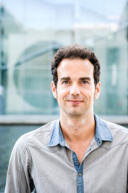 Portrait von einem vollbärtigen Mann mit kurzen Haaren, der in die Kamera lächelt. Er trägt ein Shirt mit einem Fahrrad.