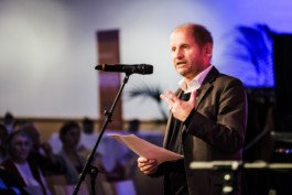 Portrait von einem vollbärtigen Mann mit kurzen Haaren, der in die Kamera lächelt. Er trägt ein Shirt mit einem Fahrrad.