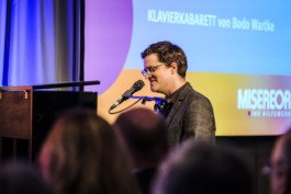 Portrait von einem vollbärtigen Mann mit kurzen Haaren, der in die Kamera lächelt. Er trägt ein Shirt mit einem Fahrrad.