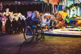 Eine Frau im Rollstuhl fährt angestrengt über einen Teer Berg auf einem Weihnachtsmarkt Portrait von einem vollbärtigen Mann mit kurzen Haaren, der in die Kamera lächelt. Er trägt ein Shirt mit einem Fahrrad.