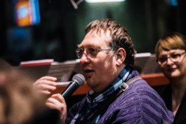 Portrait von einem vollbärtigen Mann mit kurzen Haaren, der in die Kamera lächelt. Er trägt ein Shirt mit einem Fahrrad.