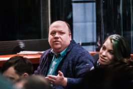 Portrait von einem vollbärtigen Mann mit kurzen Haaren, der in die Kamera lächelt. Er trägt ein Shirt mit einem Fahrrad.