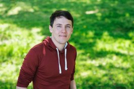 Portrait von einem vollbärtigen Mann mit kurzen Haaren, der in die Kamera lächelt. Er trägt ein Shirt mit einem Fahrrad.