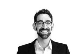 Portrait von einem vollbärtigen Mann mit kurzen Haaren, der in die Kamera lächelt. Er trägt ein Shirt mit einem Fahrrad.