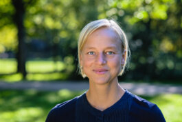 eine weiblich gelesene  blonde Person lächelt in die Kamera