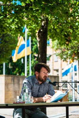Portrait von einem vollbärtigen Mann mit kurzen Haaren, der in die Kamera lächelt. Er trägt ein Shirt mit einem Fahrrad.