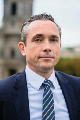 Portrait von einem vollbärtigen Mann mit kurzen Haaren, der in die Kamera lächelt. Er trägt ein Shirt mit einem Fahrrad.