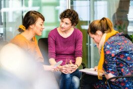 Drei weiblich gelesene Personen sitzen zusammen und besprechen ein Projekt Portrait von einem vollbärtigen Mann mit kurzen Haaren, der in die Kamera lächelt. Er trägt ein Shirt mit einem Fahrrad.